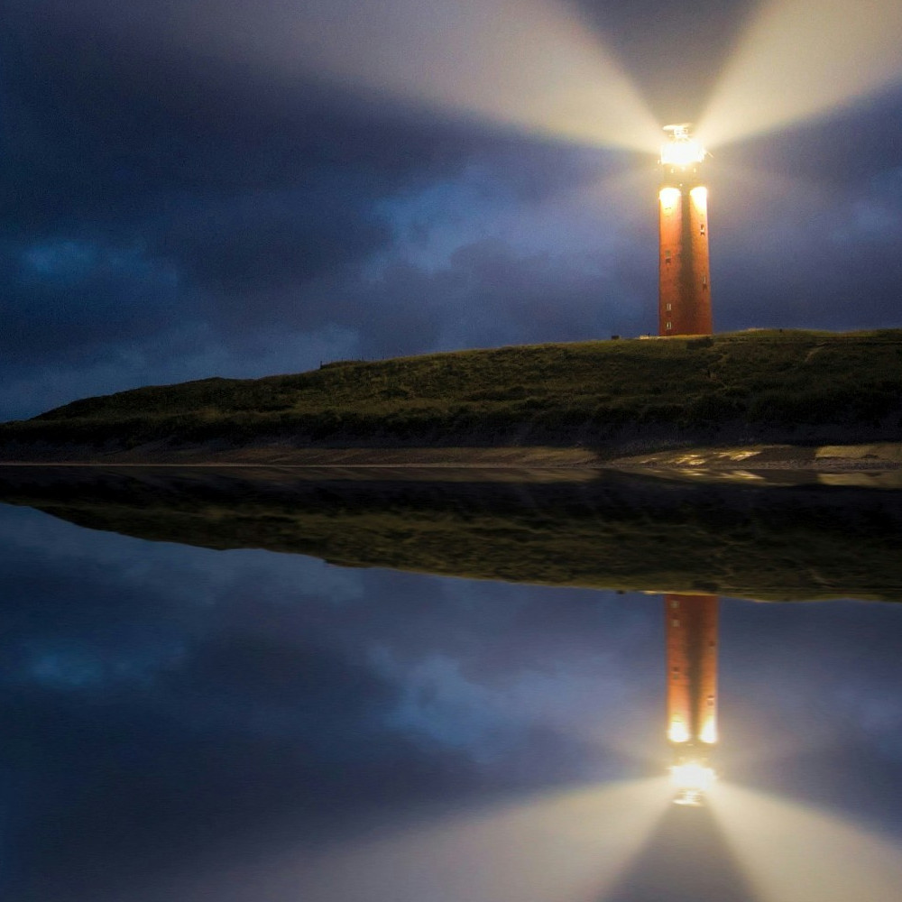 Foto eines Leuchtturms vor Abendhimmel, der sich im Wasser spiegelt.   Unsplash.com/Evgeni Tcherkasski