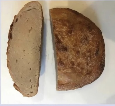 A baked round of bread without any air bubbles inside. The exterior is moderately burnt while the interior is a mass of semi-raw, burnt dough.