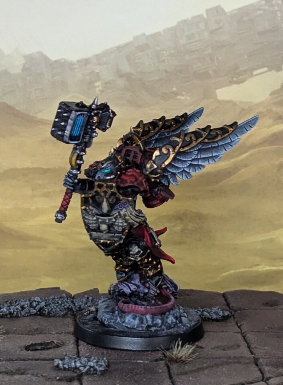 A photograph of a painted Warhammer 40,000 miniature. Black armor with red cloth and gold trim.